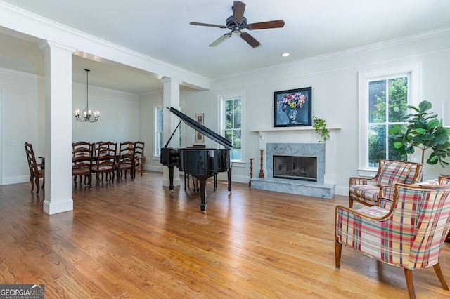 sitting room with decorative columns, wood-type flooring, ornamental molding, a premium fireplace, and ceiling fan with notable chandelier