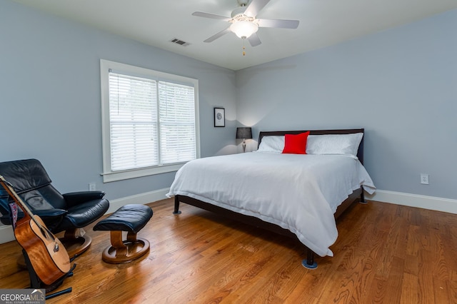 bedroom with ceiling fan, visible vents, baseboards, and wood finished floors