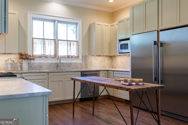 kitchen featuring crown molding, dark wood finished floors, a sink, built in appliances, and backsplash