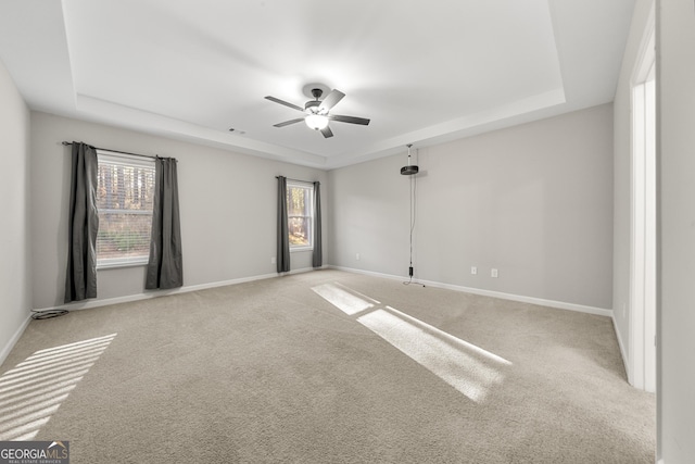 carpeted spare room with a raised ceiling, a wealth of natural light, and ceiling fan