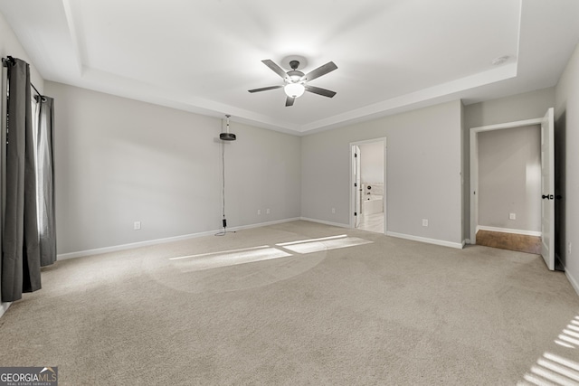 empty room with light carpet, a tray ceiling, and ceiling fan