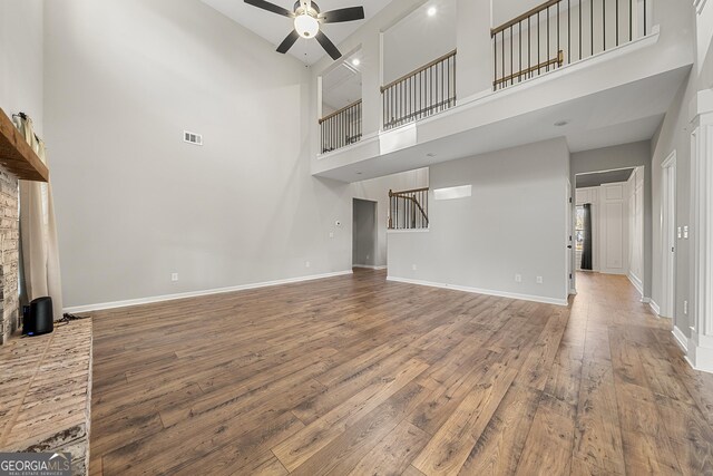 unfurnished living room with ceiling fan, wood-type flooring, and a towering ceiling