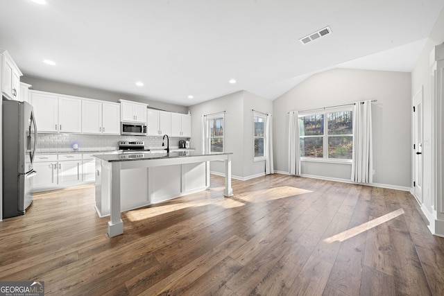 kitchen with stainless steel appliances, an island with sink, white cabinets, and backsplash