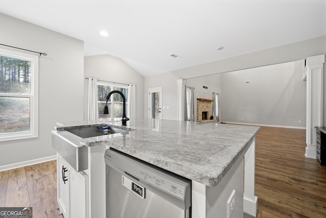 kitchen featuring a fireplace, stainless steel dishwasher, white cabinets, and a center island with sink