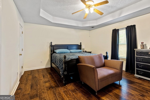 bedroom featuring ceiling fan, dark wood-type flooring, a raised ceiling, and a textured ceiling