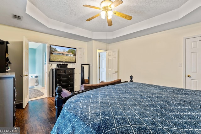 bedroom with dark wood-type flooring, ceiling fan, connected bathroom, a tray ceiling, and a textured ceiling