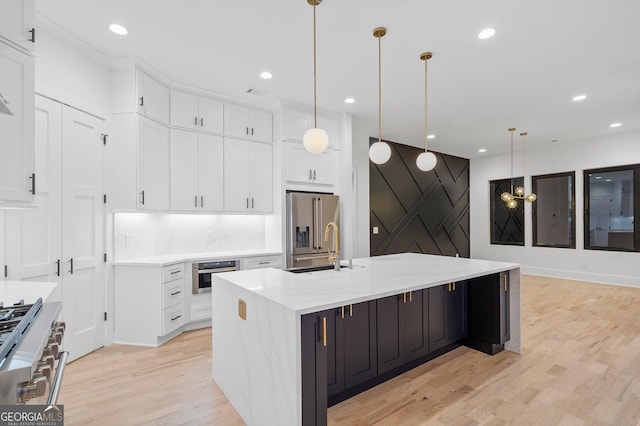 kitchen with decorative light fixtures, appliances with stainless steel finishes, white cabinets, and a center island with sink