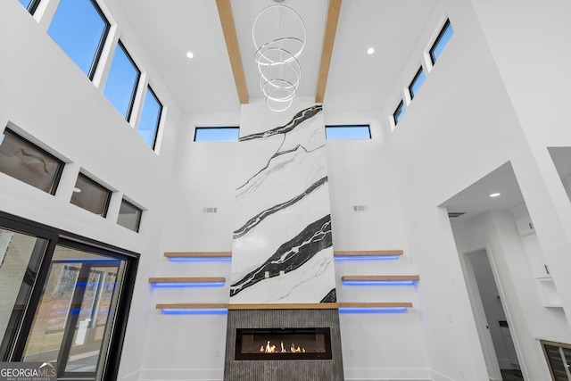 unfurnished living room with beam ceiling, a towering ceiling, a high end fireplace, and an inviting chandelier