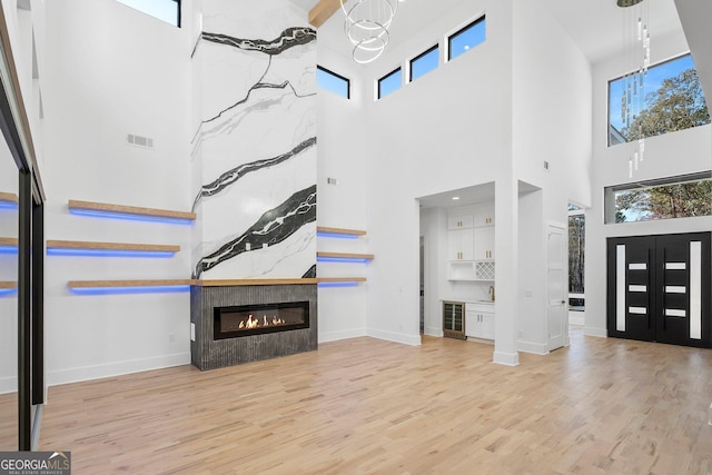 unfurnished living room featuring a fireplace, beverage cooler, a chandelier, and light wood-type flooring