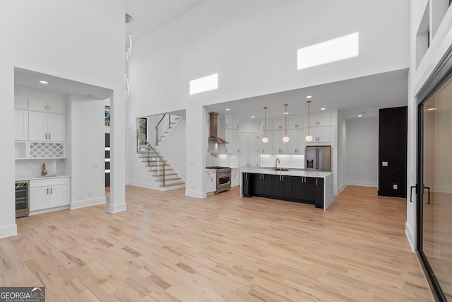 unfurnished living room with a high ceiling, wet bar, beverage cooler, and light hardwood / wood-style floors