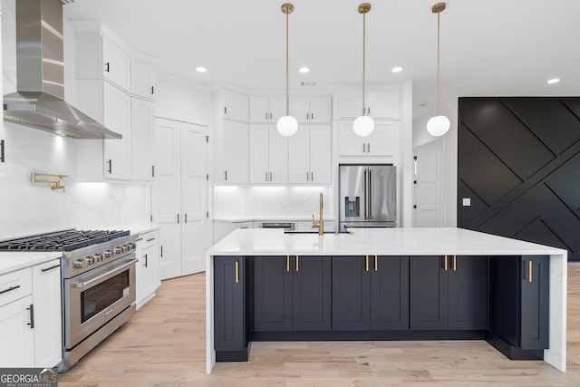 kitchen with decorative light fixtures, high quality appliances, sink, wall chimney range hood, and a center island with sink