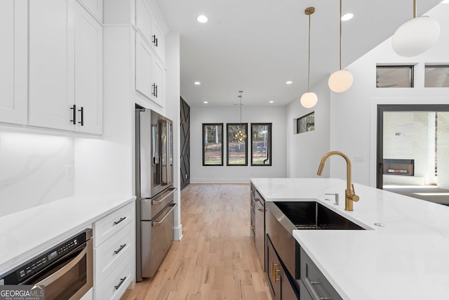 kitchen with sink, hanging light fixtures, light wood-type flooring, appliances with stainless steel finishes, and white cabinets