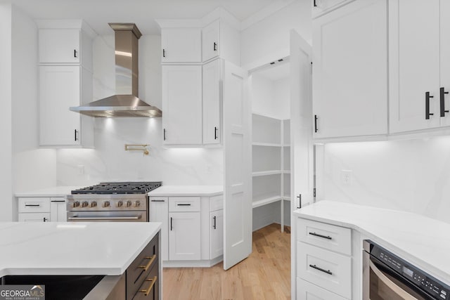 kitchen with backsplash, white cabinets, high end range, wall chimney exhaust hood, and light hardwood / wood-style flooring