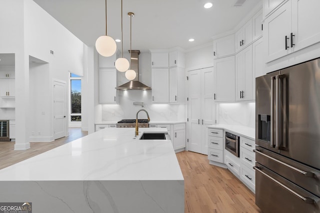 kitchen with sink, high end refrigerator, pendant lighting, wall chimney range hood, and white cabinets