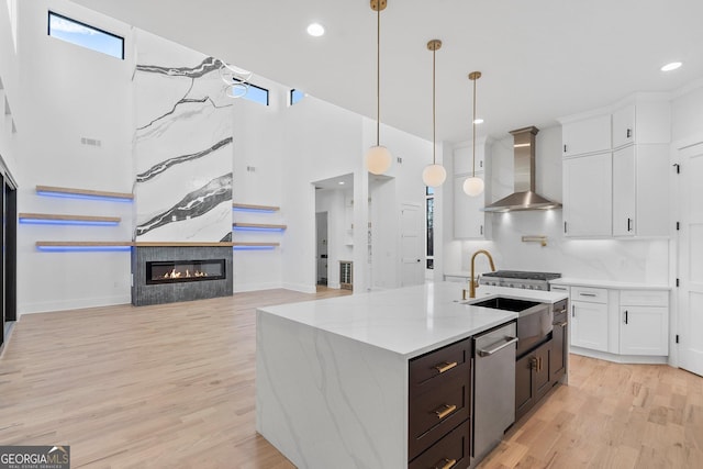 kitchen featuring pendant lighting, wall chimney range hood, appliances with stainless steel finishes, white cabinetry, and light stone counters