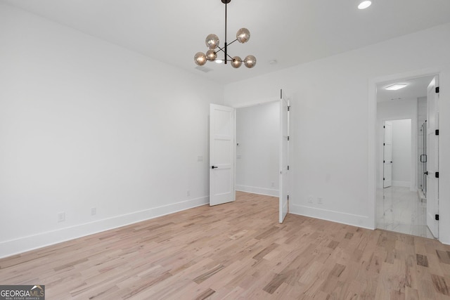 unfurnished room featuring a notable chandelier and light hardwood / wood-style flooring