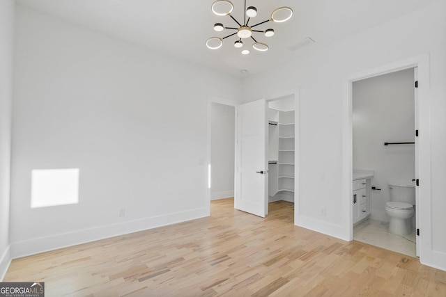 unfurnished bedroom with an inviting chandelier, ensuite bath, a spacious closet, a closet, and light hardwood / wood-style floors