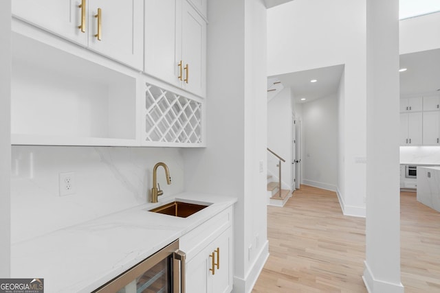 bar with sink, white cabinetry, light stone counters, light hardwood / wood-style floors, and decorative backsplash