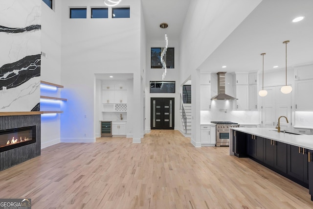 kitchen featuring wall chimney range hood, stainless steel stove, sink, white cabinets, and decorative light fixtures