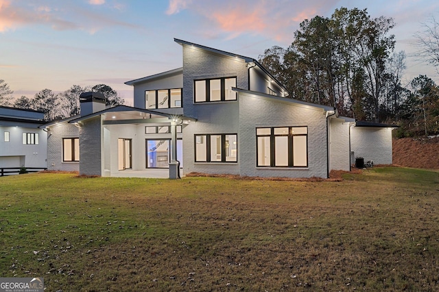 back house at dusk featuring a lawn and a patio area