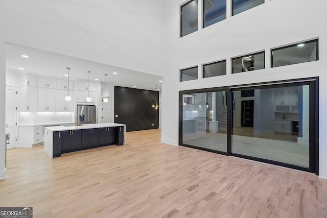 kitchen with white cabinetry, stainless steel refrigerator with ice dispenser, a kitchen island with sink, and pendant lighting