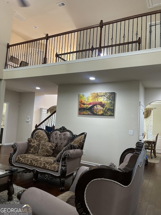 living room featuring arched walkways, wood finished floors, visible vents, a towering ceiling, and baseboards