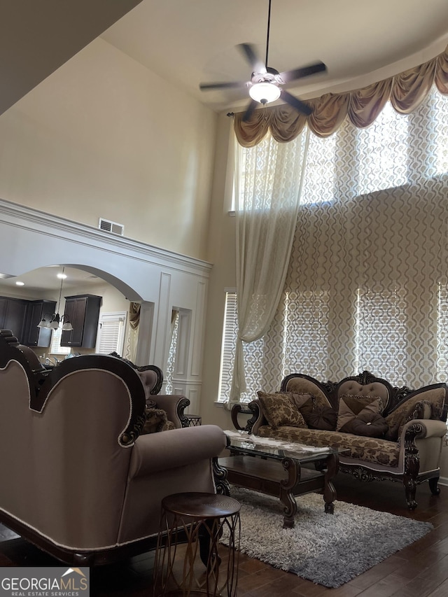 living room with arched walkways, a towering ceiling, visible vents, a ceiling fan, and dark wood-style floors