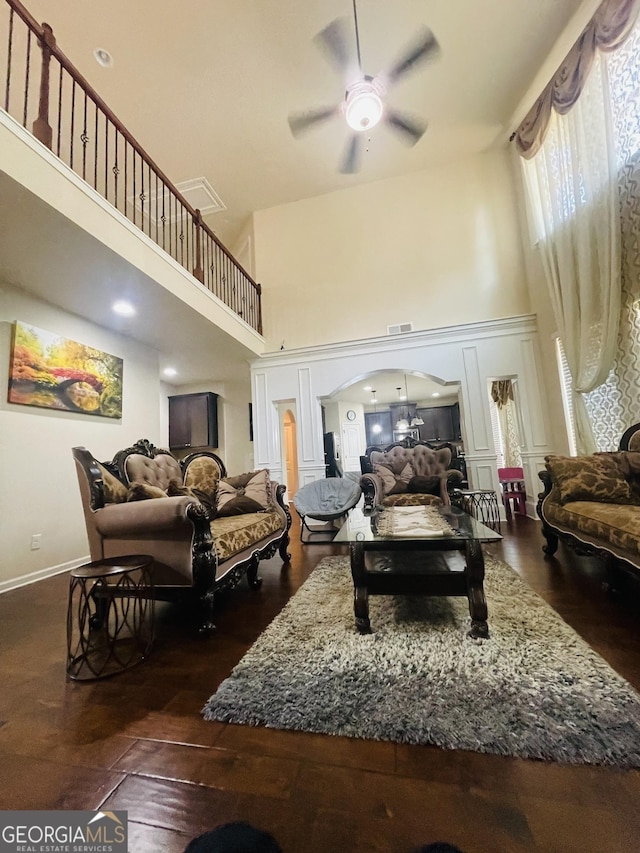 living area with a towering ceiling, dark hardwood / wood-style floors, and ceiling fan