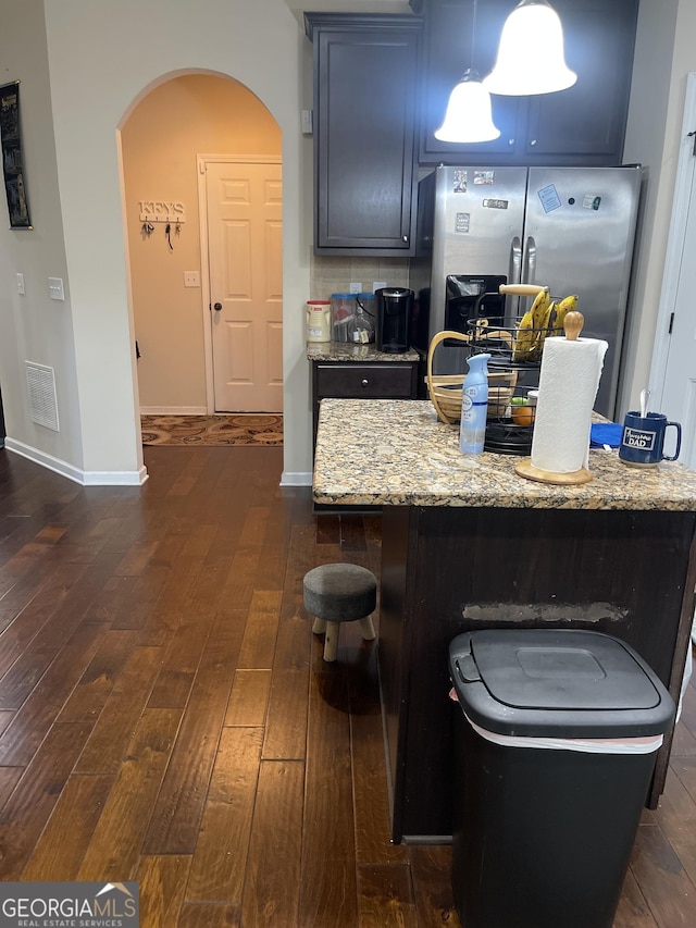 kitchen featuring arched walkways, light stone counters, dark wood-type flooring, visible vents, and stainless steel fridge with ice dispenser