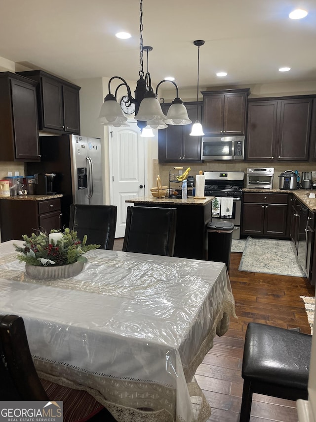 kitchen featuring dark wood-type flooring, hanging light fixtures, a kitchen island, stainless steel appliances, and light stone countertops