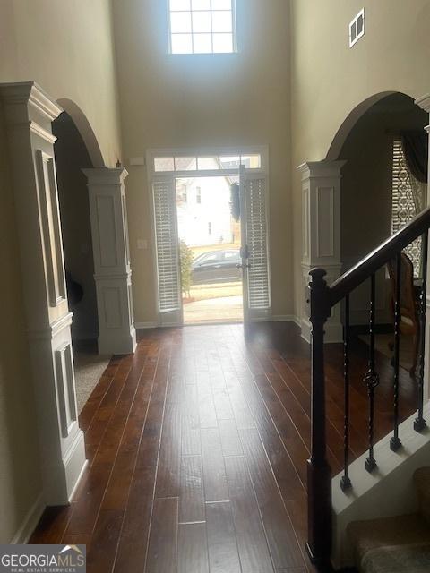 foyer entrance with dark hardwood / wood-style flooring, a towering ceiling, and ornate columns