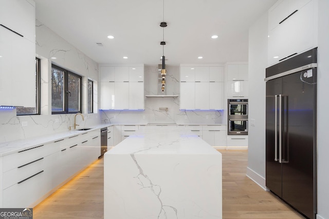 kitchen featuring white cabinetry, hanging light fixtures, light stone countertops, a kitchen island, and built in fridge