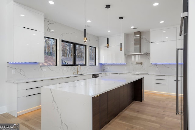 kitchen with sink, white cabinetry, decorative light fixtures, a center island, and wall chimney range hood