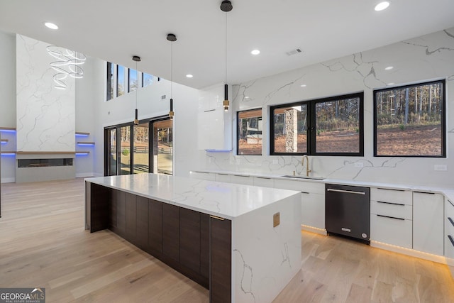 kitchen featuring decorative light fixtures, white cabinetry, sink, light stone countertops, and light wood-type flooring