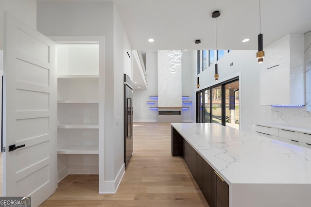 kitchen with dark brown cabinetry, white cabinetry, decorative light fixtures, light hardwood / wood-style flooring, and light stone countertops