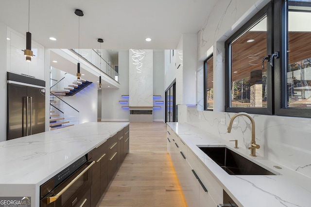 kitchen with sink, white cabinetry, high end refrigerator, decorative light fixtures, and light stone countertops