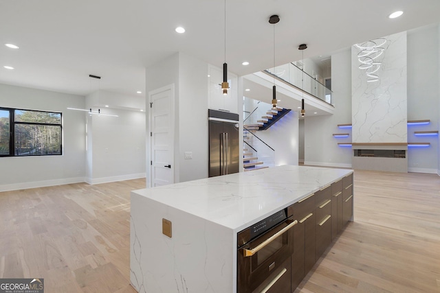 kitchen featuring black oven, hanging light fixtures, a spacious island, high quality fridge, and light wood-type flooring