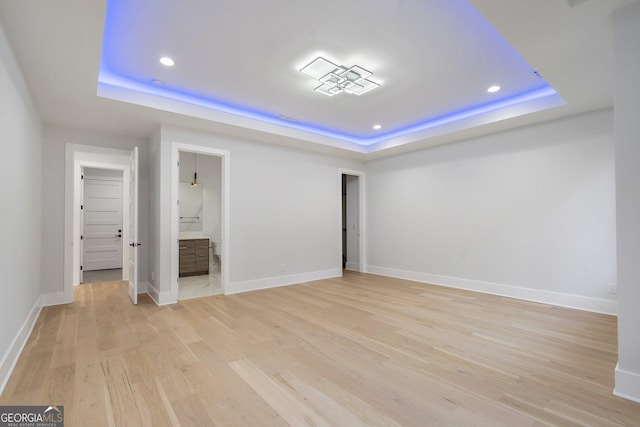 unfurnished bedroom with connected bathroom, a tray ceiling, and light hardwood / wood-style flooring