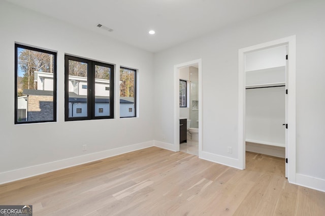 unfurnished bedroom with a walk in closet, ensuite bathroom, a closet, and light hardwood / wood-style flooring