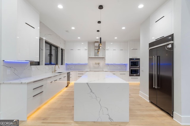 kitchen featuring white cabinetry, decorative light fixtures, a kitchen island, stainless steel appliances, and wall chimney range hood