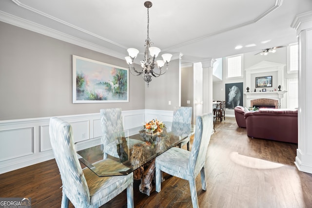 dining area featuring crown molding, dark wood-type flooring, an inviting chandelier, a fireplace, and ornate columns