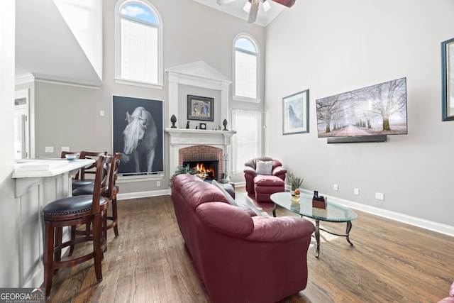 living room with a high ceiling, a brick fireplace, dark hardwood / wood-style floors, and ceiling fan