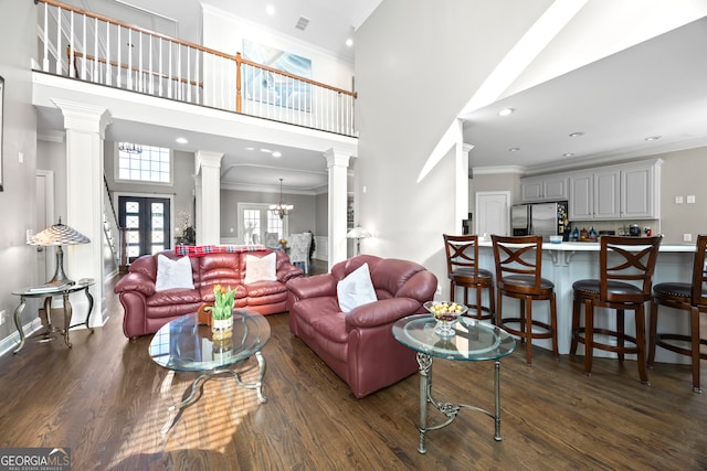 living room featuring dark wood-type flooring, an inviting chandelier, a high ceiling, and ornate columns