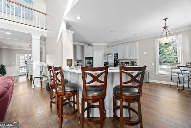 kitchen with appliances with stainless steel finishes, dark hardwood / wood-style floors, a kitchen bar, ornamental molding, and kitchen peninsula