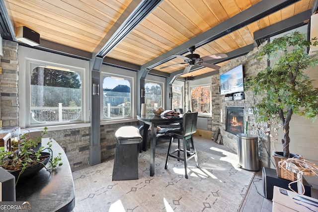 sunroom with ceiling fan, beam ceiling, wooden ceiling, and an outdoor stone fireplace