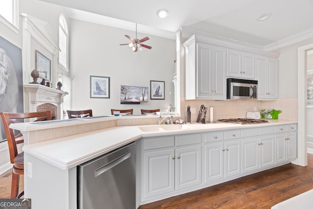 kitchen with sink, crown molding, stainless steel appliances, white cabinets, and a brick fireplace