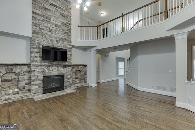 unfurnished living room with ornate columns, wood-type flooring, a stone fireplace, and ceiling fan