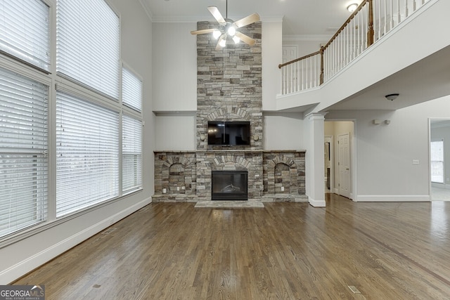 unfurnished living room with wood-type flooring, ornamental molding, a wealth of natural light, ceiling fan, and a fireplace