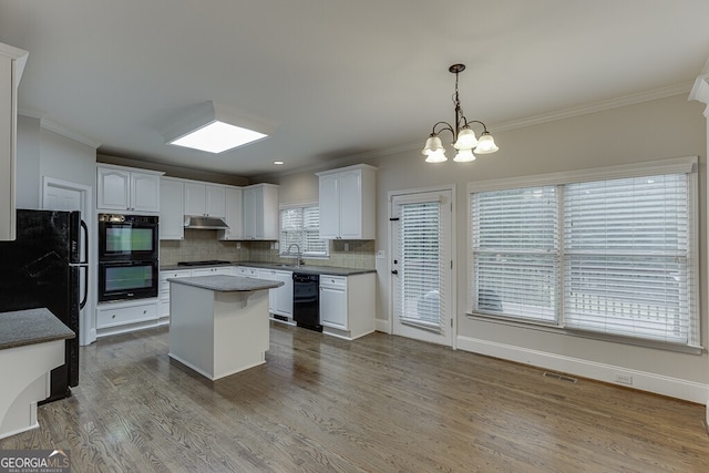 kitchen with sink, hanging light fixtures, a center island, black appliances, and white cabinets