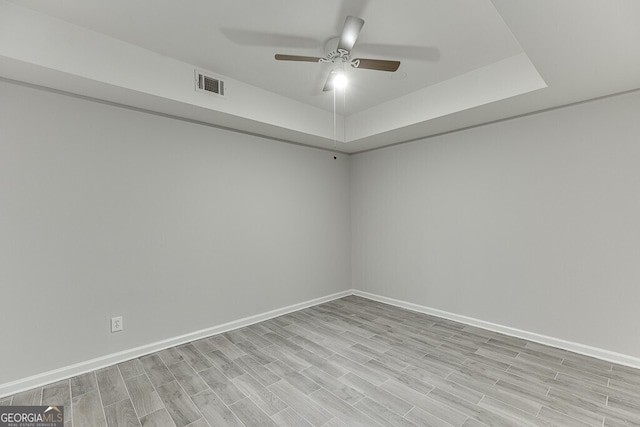 empty room featuring a tray ceiling, ceiling fan, and light hardwood / wood-style flooring